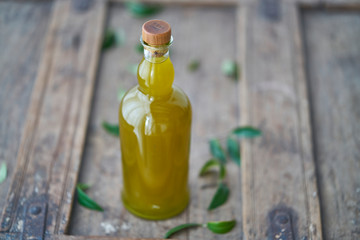 glass bottle on a wooden shabby table filled with fresh olive oil that shimmers golden yellow surrounded by green olive leaves. Wellness happiness relaxed body
