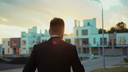 Confident businessman in suit walking along the modern street at sunset. Following attractive young...