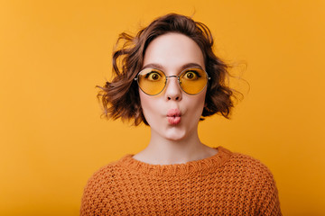 Close-up portrait of pretty girl isolated on yellow background with kissing face expression. Funny european female model with shiny hair expressing surprised emotions.