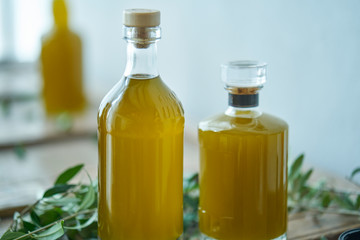 glass bottles filled with a golden liquid oil juice healthy fresh on a rustic wooden piece of furniture olive leaves around them unsharp background