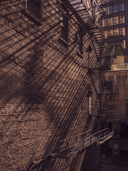 The morning sun glints through the gap in the mysterious alleyway, the metal stairway casting slanting shadows on the brick wall.