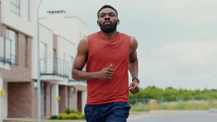Handsome fit healthy african man listening music jogging in modern street on sunny day. Portrait of focused athletic guy enjoying his running training session in the neighbourhood.