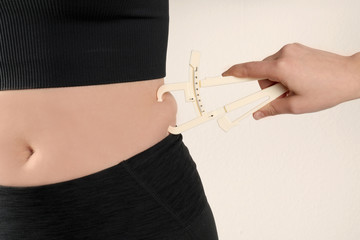 Nutritionist measuring woman's body fat layer with caliper on beige background, closeup
