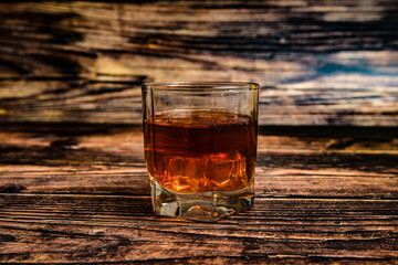 Alcohol in a glass goblet on a wooden background, cognac, whiskey, brandy with ice.