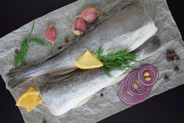 Fresh sea fish with herbs, spices and lemon on a black background.
