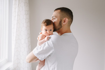Happy Caucasian father holding newborn baby. Male bearded man parent hugging kissing child daughter...