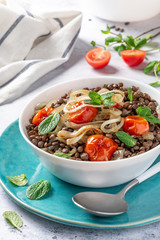 Cooked green lentils with tomatoes, onions and mint in a white bowl 