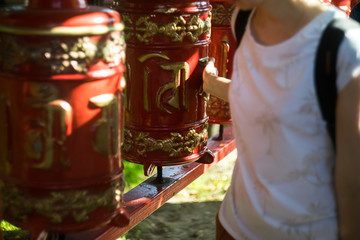.A young girl twists a prayer drum in a Buddhist temple. Red khurde in the sun. Mani drum