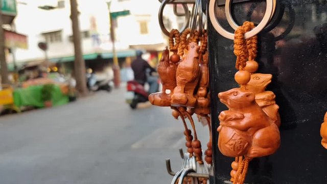 Wooden carved figurines as keyrings hanging in a Chinese night market. Busy street with scooters and motorbikes passing in the background. Wooden mouse figurine.  No people.