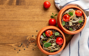 Cooked green lentils with tomatoes, onions and mint in pots on a wooden background, top view, copy space. Vegan and vegetarian food, Mediterranean cuisine.