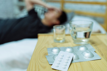 Young Asian man feeling sick and ill lying on bed with medicines tablets and pills on table. Healthcare and medicine concept