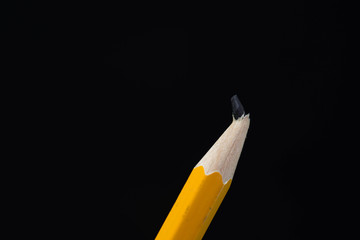 Tilted yellow broken pencil close up macro shot on black background with copy space.
