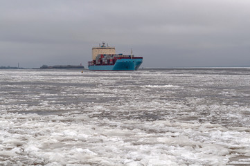 View of the ice - covered Gulf of Finland and a large ship (container ship) on a cloudy winter day