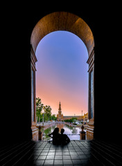 Naklejka premium Silhouettes of young couple enjoying the sunset in the famous Spain Square (Plaza de Espana). Seville, Spain.