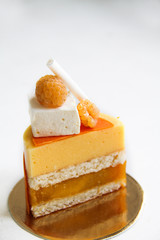 Individual cake with coconut, mango, passion fruit, yellow raspberries. Decorated with passion fruit marshmallow, meringue and raspberries. Cake is on a golden cardboard base, on a white background.