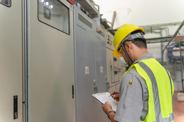 Asian electric engineer holding clipboard for checking and monitoring the electrical system in the control room,Technician thailand people working