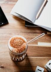 Cup of latte served with glass tube on a wooden  work desk. Coffee break concept.