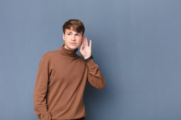 young blonde man looking serious and curious, listening, trying to hear a secret conversation or...