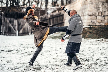 Battle of two warriors in armor with weapons fighting with swords in the snow