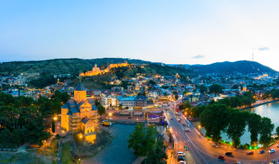 The evening panorama of the old town in the old district of Avlabari, Holy Trinity Cathedral and Rike Park, the Kura river reflects the evening city lights in Tbilisi, Georgia. © miklyxa