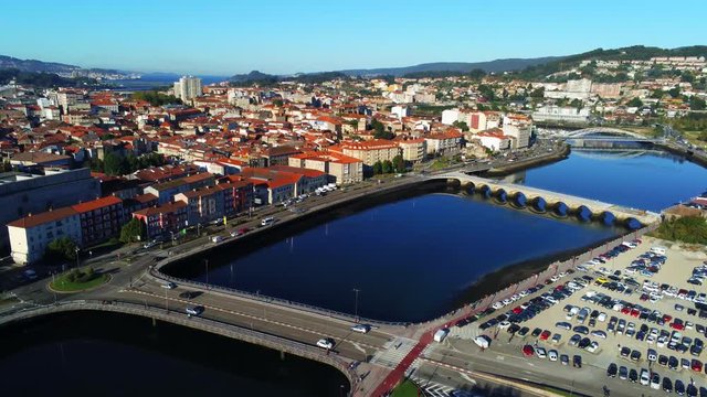 Aerial, rising, drone shot, of traffic on a bridge, the Lerez river and the cityscape of Pontevedra, at sunset, in Galicia, North Spain