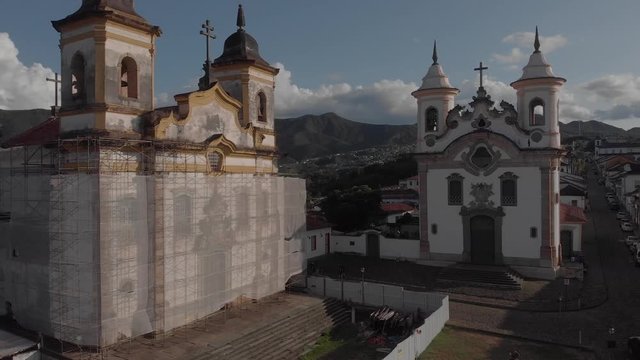 Aerial pan showing Our Lady of Carmo and San Francisco churches at central Gomes Freire square in the colonial town of Mariana in Minas Gerais, Brazil, with one of them wrapped as part of renovations