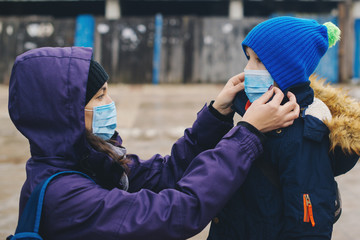 Mother puts her child a face protective mask on the street. Stop the infection. Coronavirus quarantine. Apocalypse.