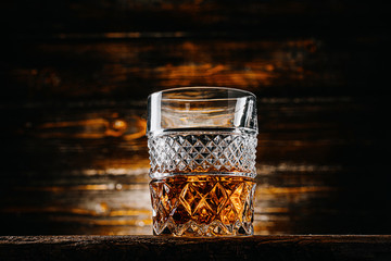 glass of whiskey with ice on a wooden table surrounded by smoke