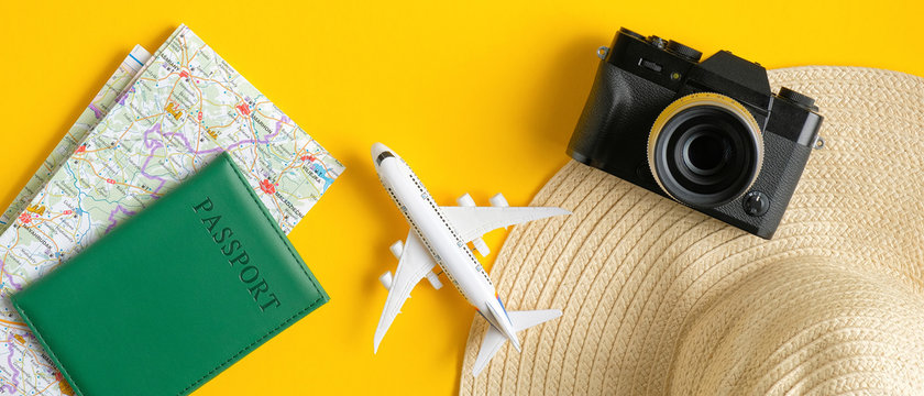 Travel accessories on yellow background. Flat lay vintage camera, beach hat, map, passport, airplane. Top view with copy space. Summer holiday travel planning concept