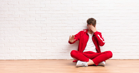 young blonde man covering face with hand and putting other hand up front to stop camera, refusing...