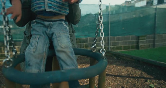 Mother lifting preschooler into swing at the playground