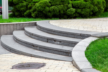 Obraz premium a staircase with granite stone steps in the park with a rectangular pavement and green lawns with bushes, close up.