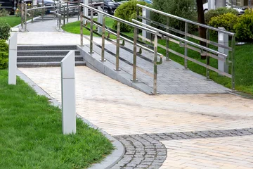 Fotobehang a stone ramp with iron railings to move people with disabilities in the city park with landscaping and steps, nobody. © Александр Беспалый