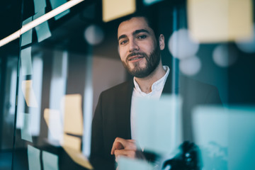 Cheerful man looking through glass board in office