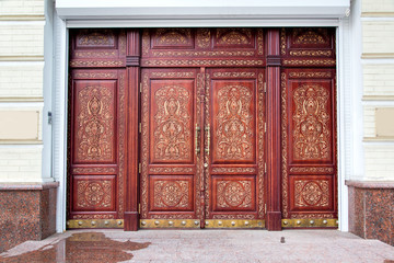 brown entrance doors on the facade of the building with stone sills and a pattern of wood carvings...