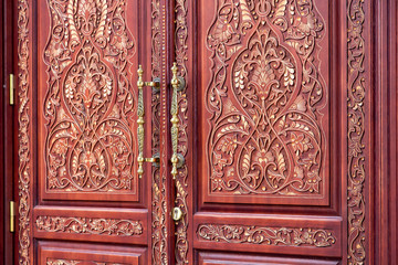 brown front door with a pattern of wood carvings with iron handles and keyhole, close up details.