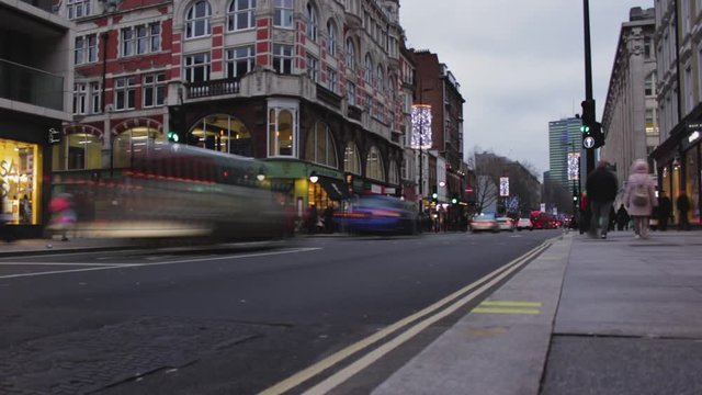 Timelapse, London red bus passing by the camera from left to right. People walking on sidewalk in winter. Cars crossing the street in the city center, London, United Kingdom