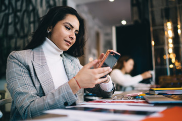 Millennial female blogger in stylish clothing checking smartphone notification for update cell application, Caucasian woman connecting to 4g wireless for installing communication app to cellphone