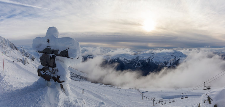 Whistler, British Columbia, Canada. Beautiful Panoramic View of Statue on top of Blackcomb Mountain with the Canadian Snow Covered Landscape in background during a cloudy and vibrant winter sunset.