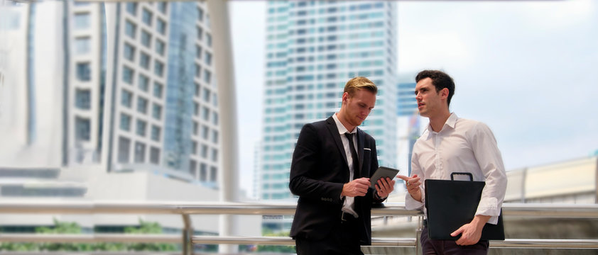 Businessman discussing and looking at mobile phone on project outside office building, urban background