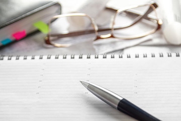 Notebook, pen, glasses, financial documents on the table. Light background.