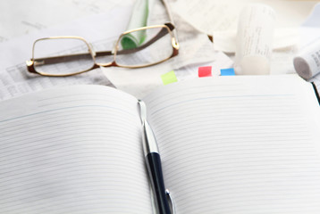 Notebook, pen, glasses, financial documents on the table. Light background.