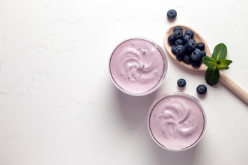 two fresh blueberry yogurt with blueberries on a white texture table, top view