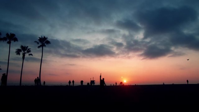 Wide point of view shot of people in silhouette on Venice beach, California under sunset.