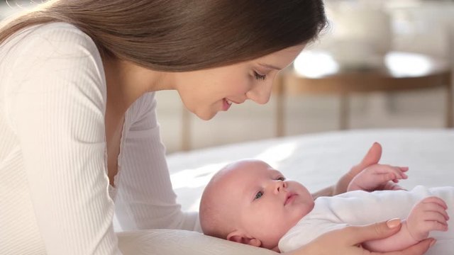 Happy family. Portrait of mother and newborn baby girl kissing hugging in bed. Maternity Parenthood Motherhood. Loving mom enjoying caring playing with little child. healthy childcare. 4 K Slow-motion