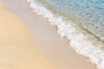 Transparent sea waves with white foam and clean yellow sand. Summer background.  Sea coast with a beautiful soft wave. blue sea wave with white foam on a clean sandy shore, selective focus. 