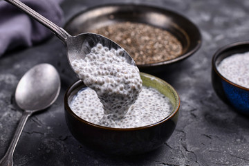 Spoon filled with chia seed pudding made with dry seeds soaked in milk in small bowls with dry...
