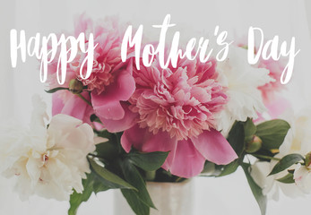 Happy Mother's day text handwritten on lovely peony bouquet in sunny light on rustic window sill. Stylish pink and white peonies in vase. Happy Mothers day greeting card