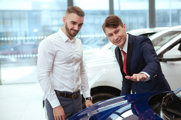 Handsome young man examining cars on sale at the dealership, talking to the salesman