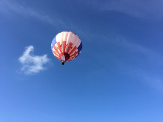Single red, white and blue hot air balloon floating up into a blue sky, further